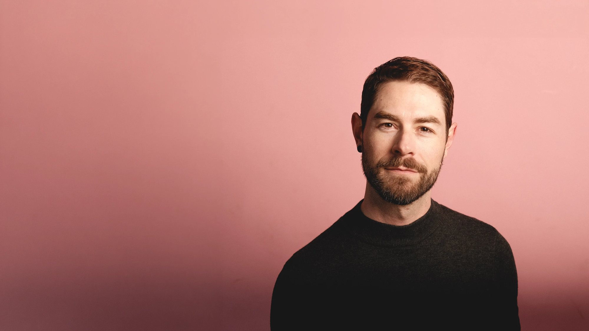 Manuel Betancourt in a black sweater against a pink wall